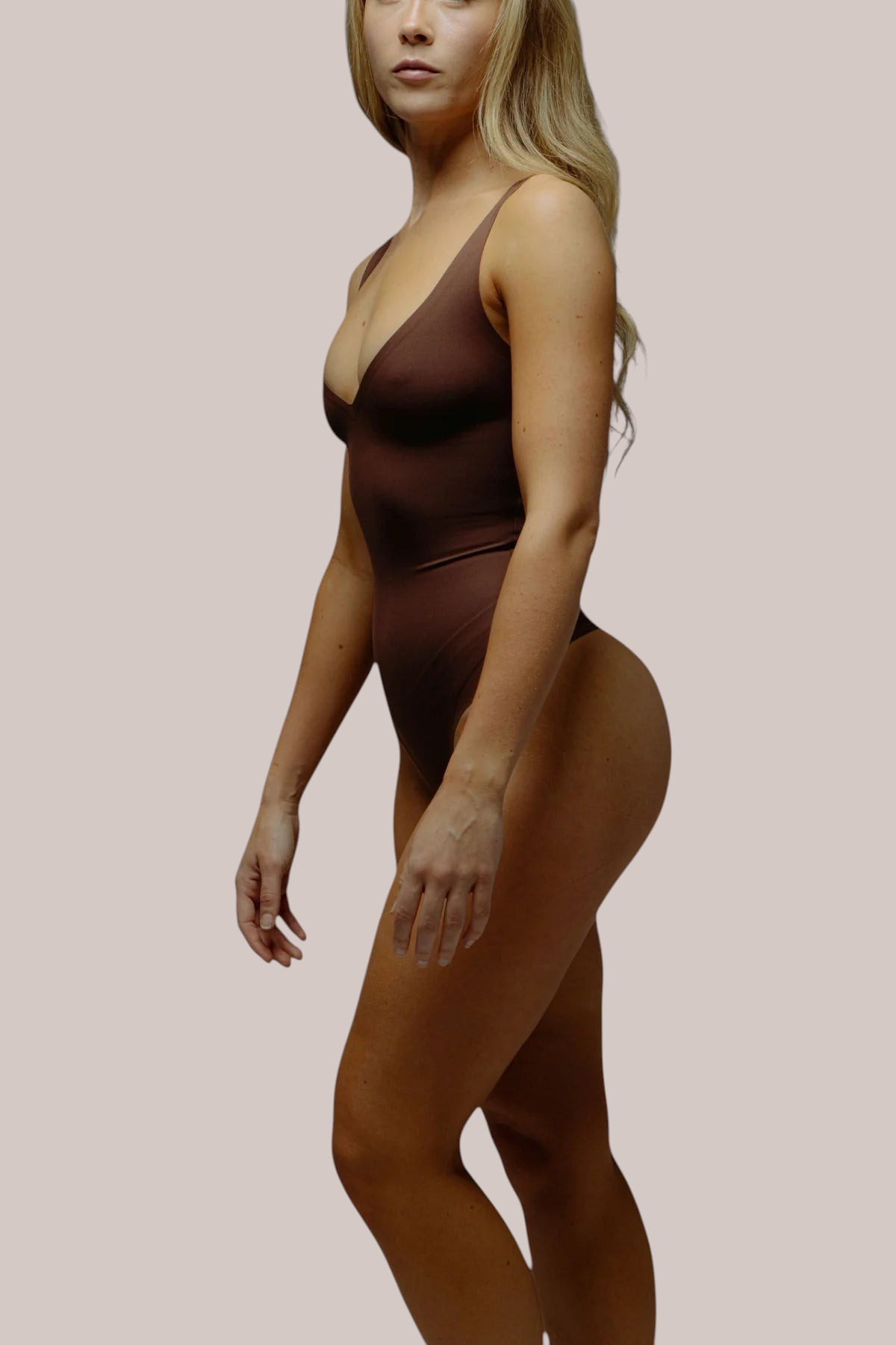 Inshapewear™ seamless brown sculpting bodysuit with a deep V-neckline and thong back on a model, side profile view.