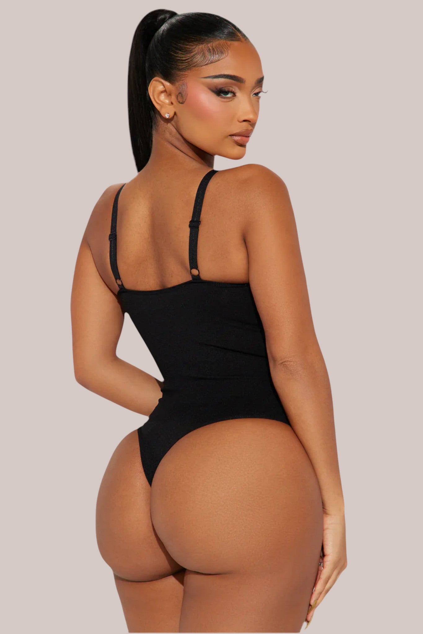 Model wearing a black Inshapewear™ thong bodysuit that provides targeted compression and a smooth silhouette.