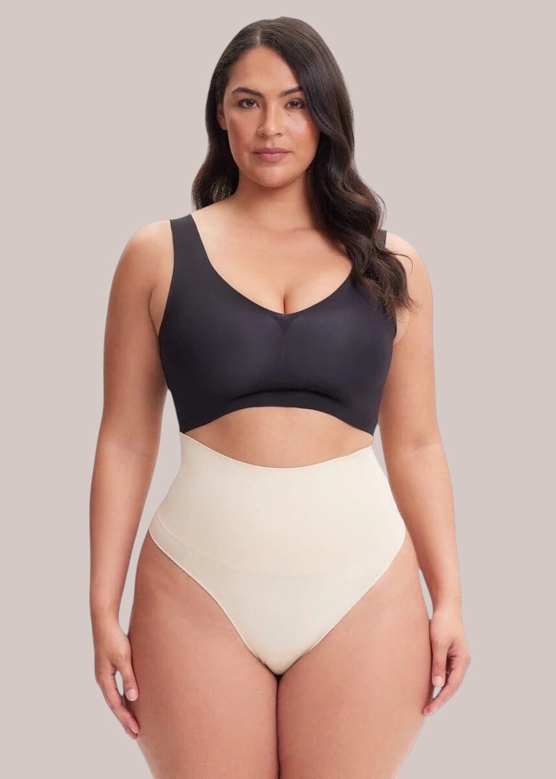 Model wearing an Inshapewear™ high-waisted beige shaping thong with a black bra against a neutral background