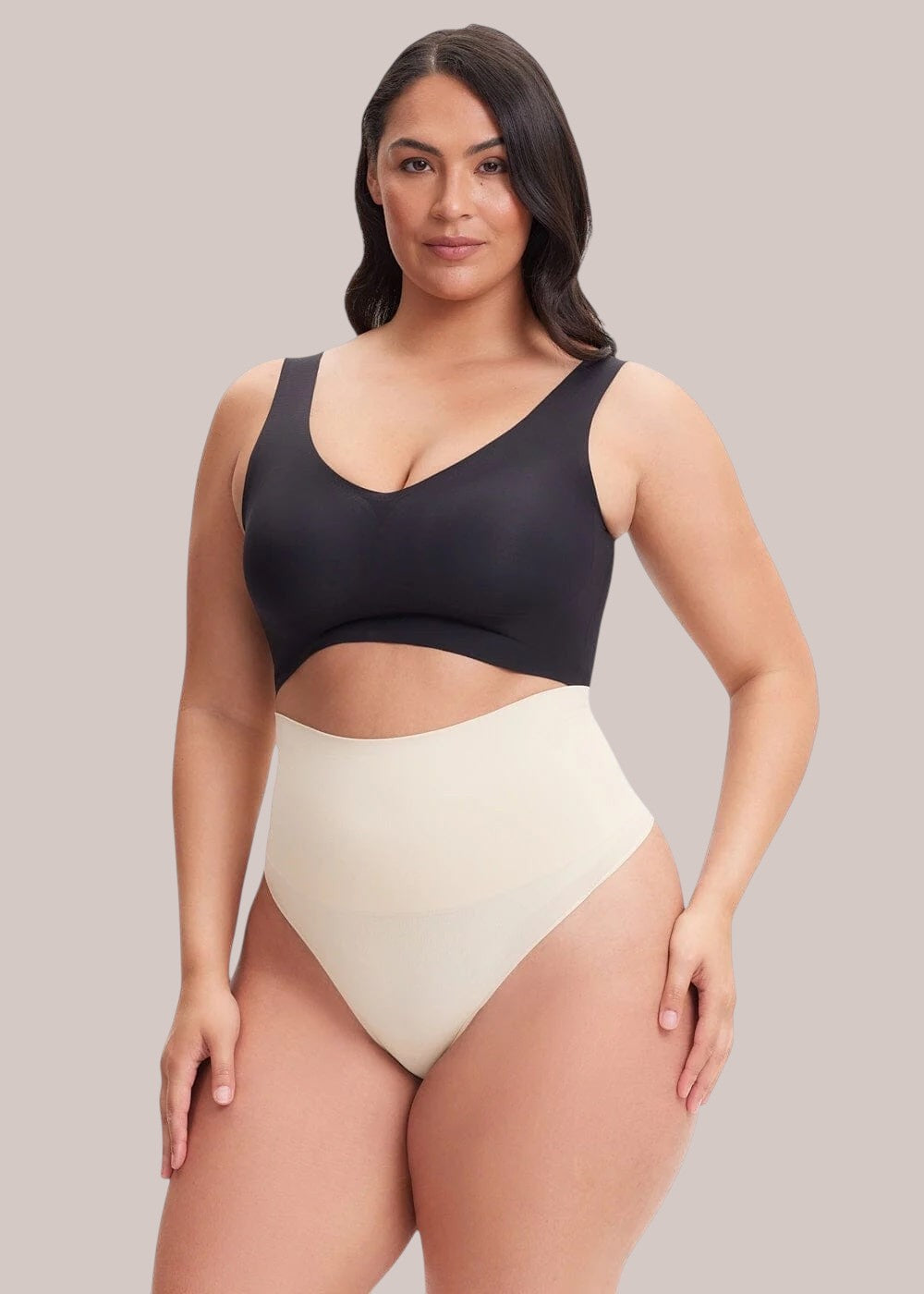 Model wearing an Inshapewear™ high-waisted beige shaping thong with a black bra against a neutral background.