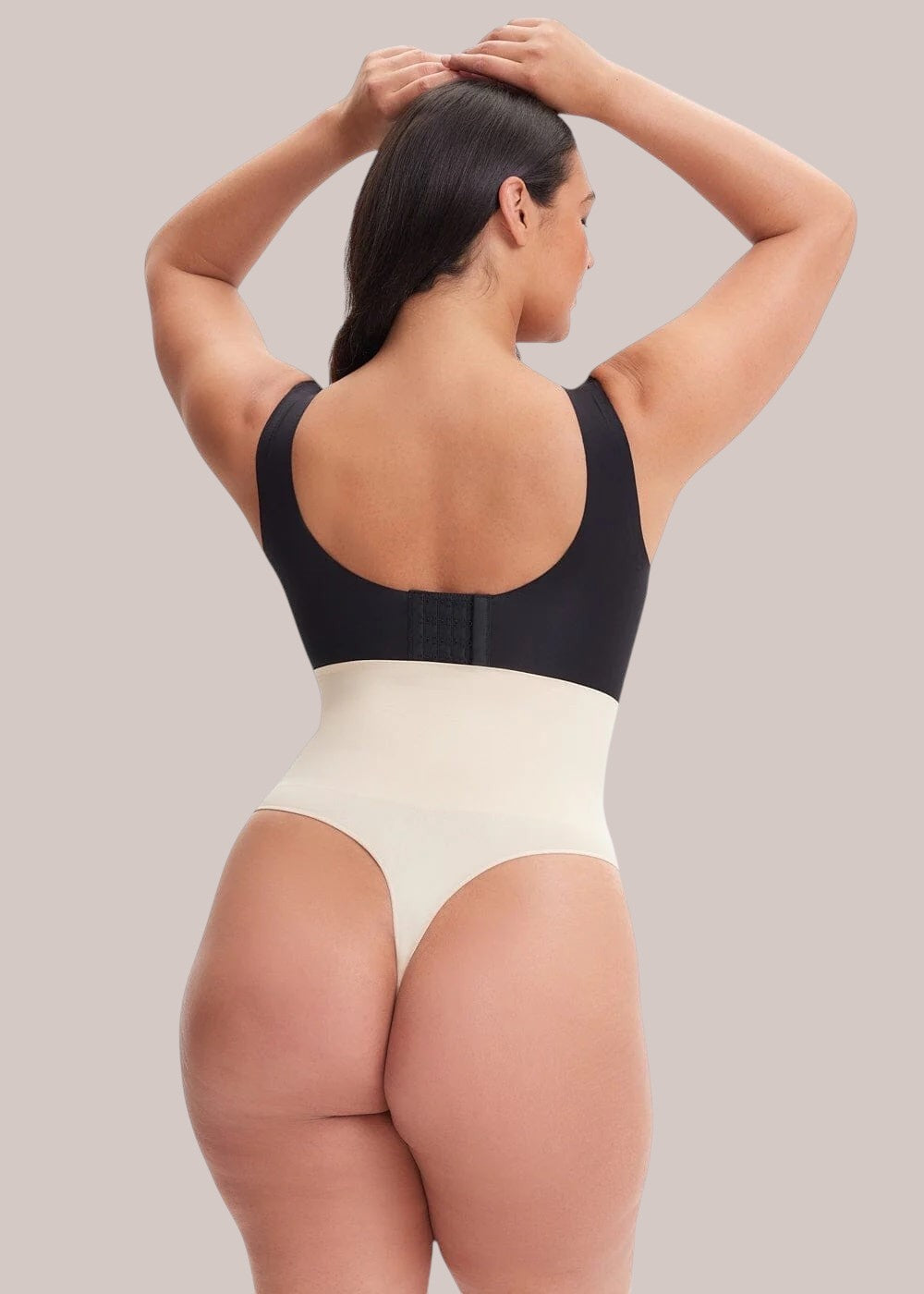 Back view of a model wearing an Inshapewear™ high-waisted beige and black thong shapewear bodysuit